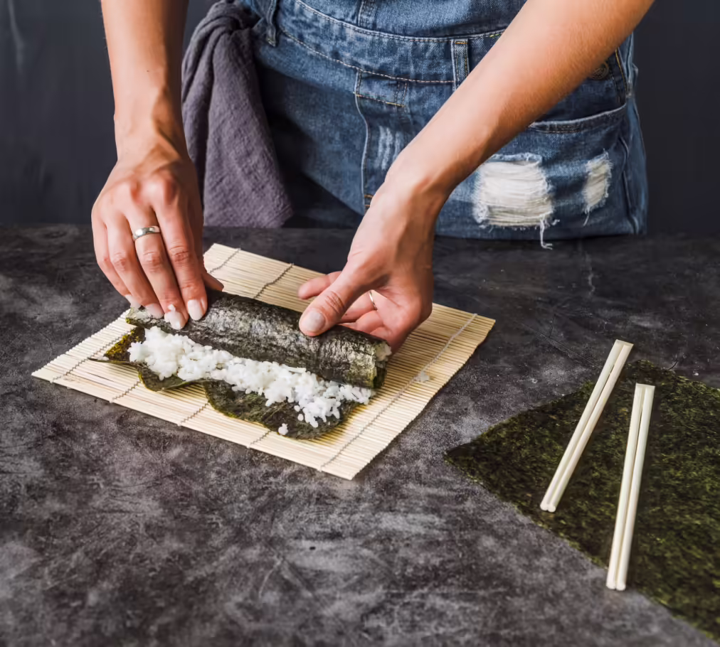 woman preparing sushi rolling a nori seaweed sheet